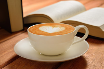 A cup of cafe latte and books on wooden table
