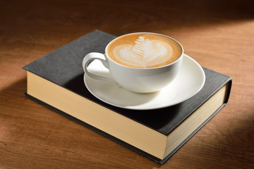 A cup of cafe latte and book on wooden table
