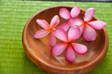 Four red frangipani flower in wooden bowl on straw mat