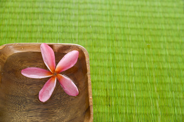 frangipani flower in water wooden bowl on green straw mat