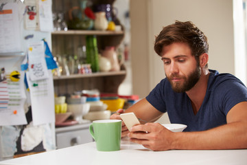 Fototapeta na wymiar Man Eating Breakfast Whilst Using Mobile Phone