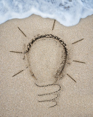 Light bulb drawn on sand beach with white wave foam