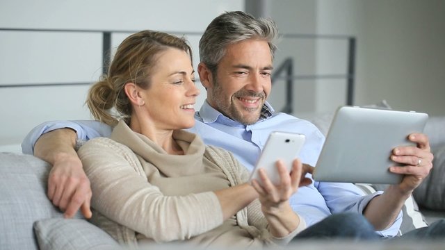 Mature couple at home using tablet and smartphone