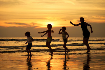 Mother and  children playing on the beach at sunset time.