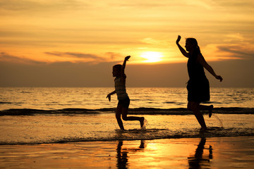 Mother and daughter playing on the beach at the sunset time.