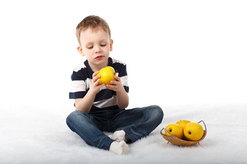 Little cute boy eating a yellow apple and smiling on white backg