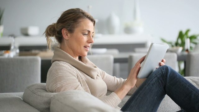 Mature woman sitting in sofa and websurfing on digital tablet