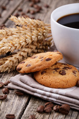 Cup of coffee with cookies and wheat on a wooden table.
