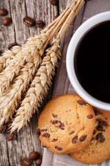 Cup of coffee with cookies and wheat on a wooden table.