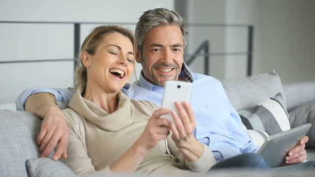 Mature couple at home using tablet and smartphone