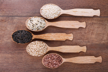 Different kinds of rice in spoons on wooden background