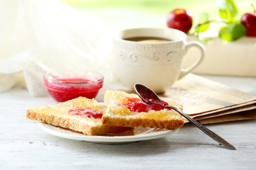 Toasts with jam on plate and cup of tea on bright background