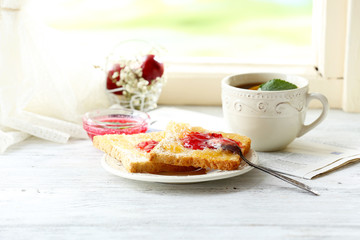Toasts with jam on plate and cup of tea on light background