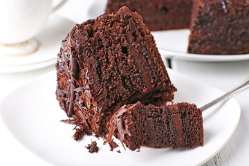 Sliced tasty chocolate cake in plate on wooden table, closeup