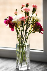 Fototapeta na wymiar Beautiful spring flowers in glass vase on windowsill background