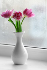 Beautiful pink tulips in vase on windowsill background