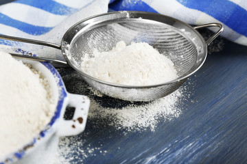 Sifting flour through sieve on wooden table, closeup