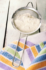 Sifting flour through sieve on wooden table, closeup