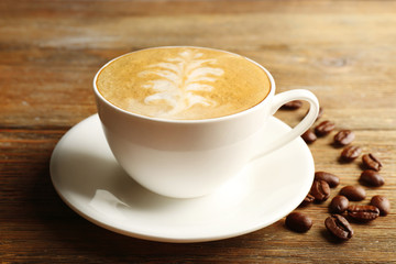 Cup of latte art coffee with grains on wooden background