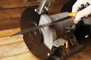 Knife sharpener and hand with blade on wooden table, closeup