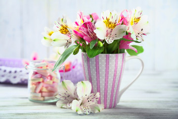 Beautiful flowers in cup, on wooden background