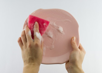 Fototapeta premium Female hand with red sponge washing pink plate 