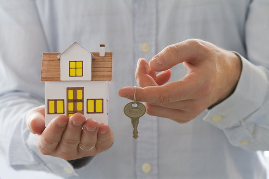 Mortgage concept. Businessman holding toy house and key in hand