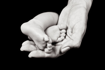Black and white close up of mother's hand holding baby's feet