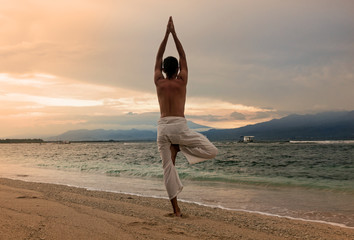 Man doing yoga on the sand beach with sunset
