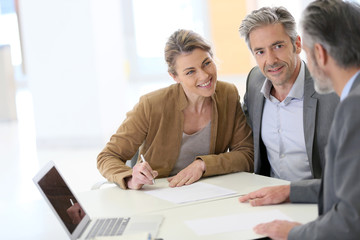 Mature couple signing financial contract at the bank - obrazy, fototapety, plakaty