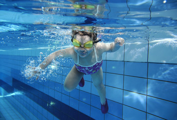 funny happy toddler girl swimming underwater in a pool with lots