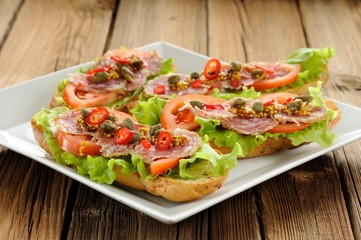 Sandwiches with ham, salad leaves, chili, tomatoes, capers, fren