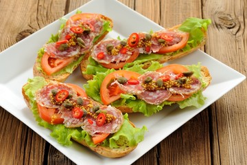 Sandwiches with ham, salad leaves, chili, tomatoes, capers, fren