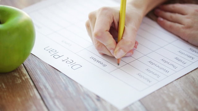 close up of young woman writing diet plan at home