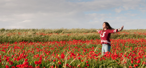 Happy Teenage Girl standing  in a red field of poppy flowers