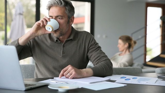 Man drinking coffee in front of laptop at home