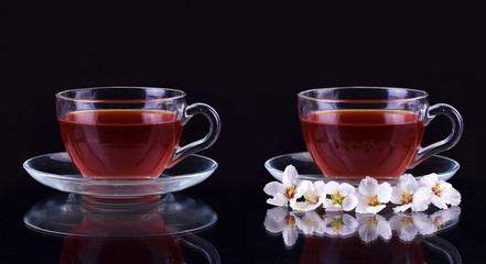cup of black tea with cherry branch flowers on dark background