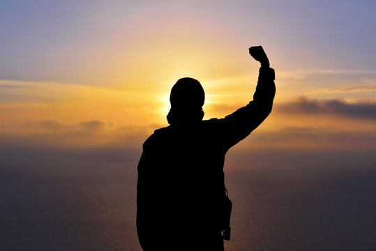 Young man standing with arms outstretched at sunset