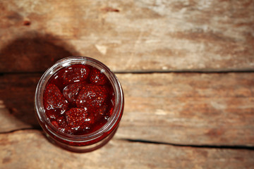 Jar of strawberry jam on wooden background