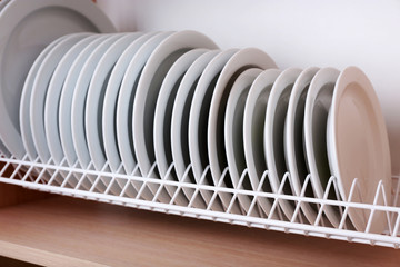 Clean plates drying on metal dish rack on shelf