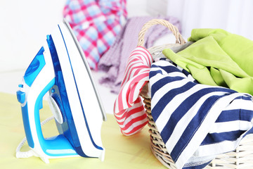 Iron and clothes on ironing board on interior background