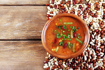 Bean soup in bowl and raw beans on wooden table background