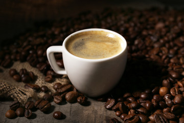 Cup of coffee and grains on wooden table with sackcloth,