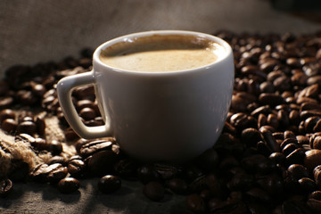 Cup of coffee and grains on wooden table with sackcloth,
