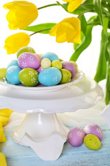 Easter eggs on vase and tulips on table on bright background