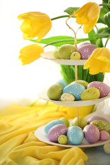 Easter eggs on vase and tulips on table on bright background