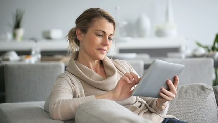 Mature woman sitting in sofa and websurfing on digital tablet - Powered by Adobe