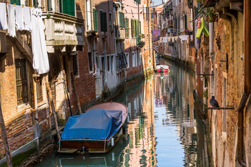 Fototapeta na wymiar Boats with tarpaulin in romantic narrow canal in Venice.