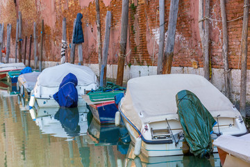 Boats with tarpaulin in romantic narrow canal in Venice.