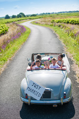 A newlywed couple is driving a retro car with their kids